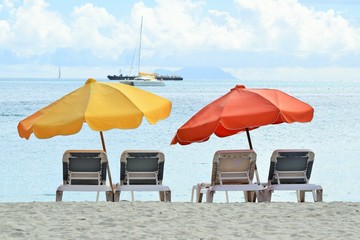 Sonnenliegen und Sonnenschirme am Strand von Miami, South Beach, Florida, USA mit Motorkatamaran und Segelboot im Hintergrund