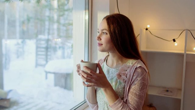 Beautiful Girl Drinking Morning Coffee or tea and looking out the window. Beauty young woman enjoying tea or coffee. 