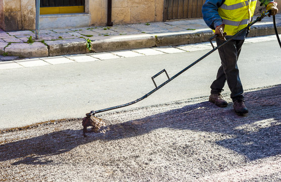 Road worker spraying bitumen emulsion with the hand spray lance before applying a new layer of asphalt