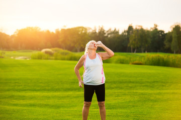 Woman drinking water from bottle. Lady standing on green grass. Training is finished. Tiredness and thirst.