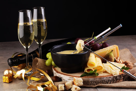 Gourmet Swiss fondue dinner on a winter evening with assorted cheeses on a board alongside a heated pot of cheese fondue with two forks dipping bread and white wine behind in a tavern or restaurant