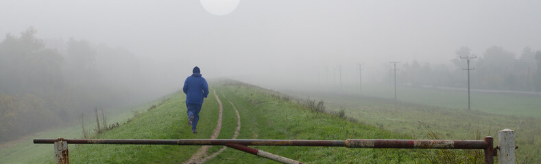 Fototapeta na wymiar Young man jogging in nature on cold misty autumn day