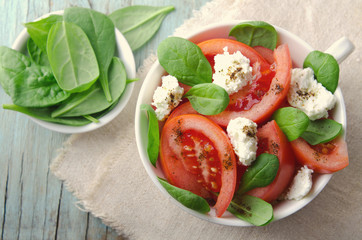 Tomato salad with spinach, cottage cheese, olive oil and pepper on blue wooden background