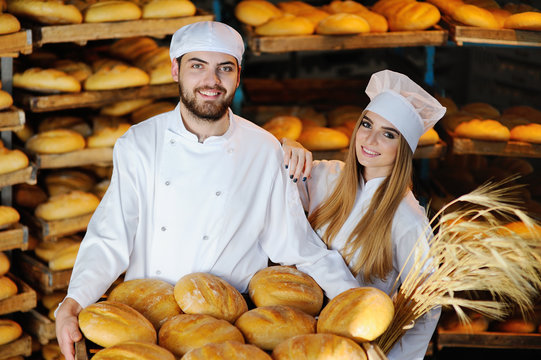 young man and woman in uniform bakers with spikelets of wheat in the hands on the background of the bakery