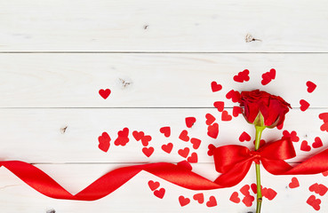 Single red rose on white wooden background with ribbon and confetti hearts