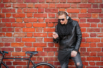 Fototapeta na wymiar Hipster man with bicycle standing by the brick wall and listening to music