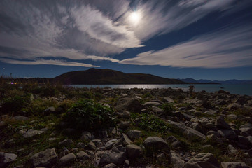 The rocky shore of Lake Tekapo under the moon light with Southern Alps in the background