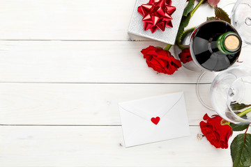 Composition of bottle of red wine on white wooden background with gifts and rose