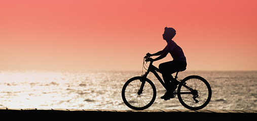 Fototapeta na wymiar Silhouette of young boy cyclist on sunset, along seashore 