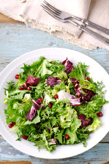 Green salad with spinach, frisee, arugula, radicchio and pomegranate seeds on blue wooden background