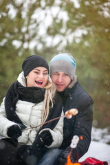 Couple embracing sitting near the fire in the winter, it is snowing, lit sparklers, roast marshmallows