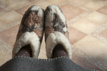 Fototapeta na wymiar Legs in home wool fur boots under a gray blanket. Close-up.