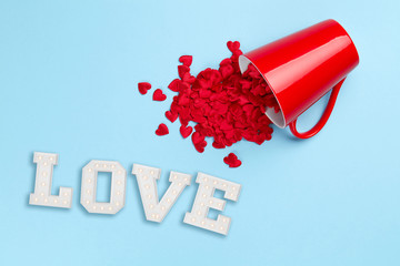 Plain blue background with love and composition of hearts spilling from red mug