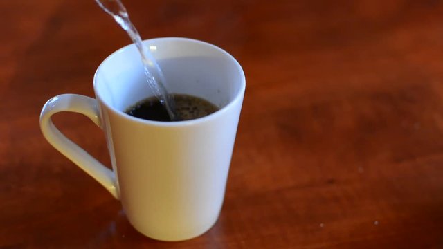 Pouring hot water into a white cup with an instant coffee.
