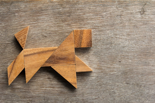 Wooden tangram as running dog shape on old wood background