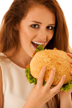 Unhealthy meal - happy young woman eats hamburger isolated over