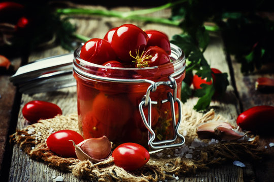 Pickled red cherry tomatoes in a glass jar on the old wooden bac