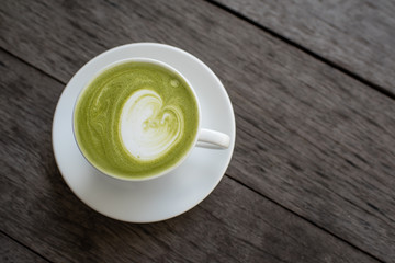 matcha green tea latte with heart shape latte art in white cup on wooden table