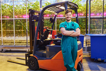 Young attractive man near electric forklift in greenhouse