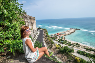 Cheering young sexy caucasian woman on the cliff of mountain. Tropical Bali island, Indonesia, Asia.