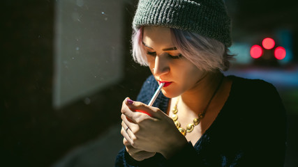 Portrait of a girl with a cigarette. young beautiful girl hipster with dyed hair smoking a cigarette in the street under the snow. her hands lights a lighter, lighting a cigarette tobacco