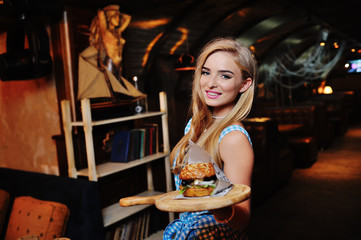 pretty girl waiter holding a delicious burger on a tray on a background of the restaurant