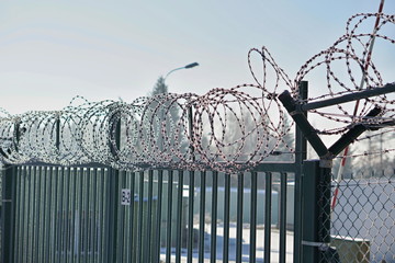 High metal fence with a sharp barbed wire on the top covered by snow in winter as a symbol of...