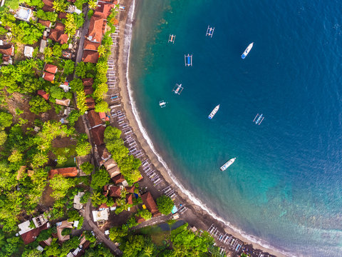 Aerial shot of calm lagoon with traditional boats and buildings on the shore. Bali, Indonesia