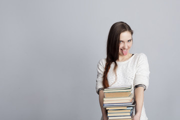 Girl with a stack of books showing tongue. Joking during study