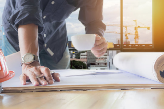 Image of engineer holding a cup of coffee and check blue print a