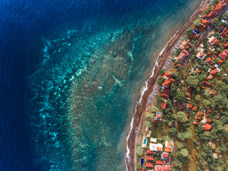 Aerial shot of underwater coral reef near shore with buildings. Bali, Indonesia