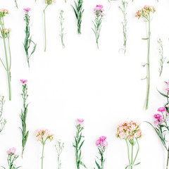 Frame with colorful wildflowers, green leaves, branches on white background. Flat lay, top view. Valentine's background