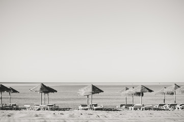 Holiday and vocation image with sandy beach, parasol and chairs on outdoors background. Black and white image