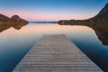 Wooden pier on a blue lake sunset and smooth reflection on water. Long exposure; Borovoye Lake;...