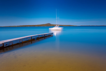 Obraz premium Blurred silhouette of white yacht moored to the lake pier. Long exposure shot.