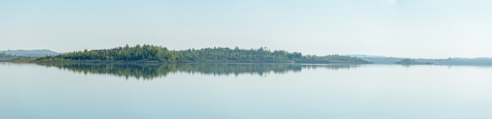 Ultra-wide panorama of lake coast line at the morning. Reflections of the trees at the water surface look like sound wave histogram.