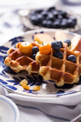 Blueberry apple waffle with honey set on a dish decorated with fresh blueberry, apple, tea pot set ready to serve.