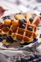 Blueberry apple waffle with honey set on a dish decorated with fresh blueberry, apple, tea pot set ready to serve.