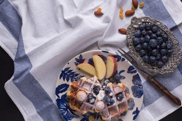 Blueberry apple waffle with honey set on a dish decorated with fresh blueberry, apple, tea pot set ready to serve.