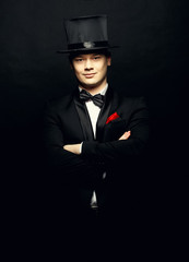 A magician in a black suit holding an empty top hat and magic wand isolated on black background