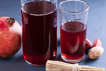 Fresh pomegranate and pomegranate juice in a transparent glass with decor nutmeg and dried herbs on a dark background