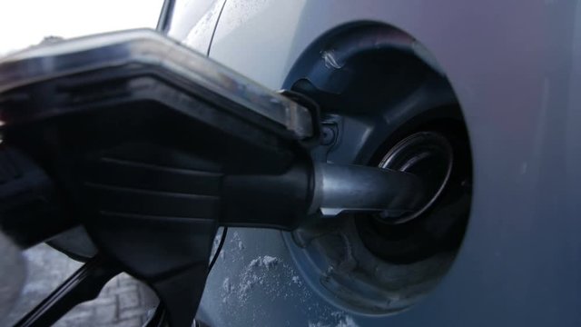 Filling car with gas fuel at station pump. Blue car, winter. Hand with gloves.