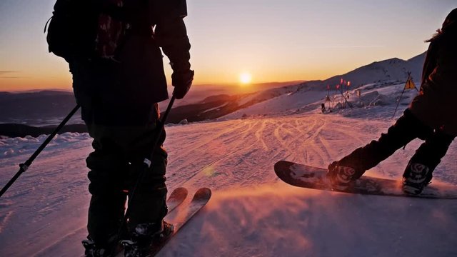 Slowmotion footage of a skier and snowboarder riding the slope during a beautiful sunset.