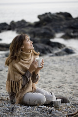 femme assise sur la plage avec une tasse en hiver