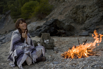 femme souriante qui campe dehors au coin du feu