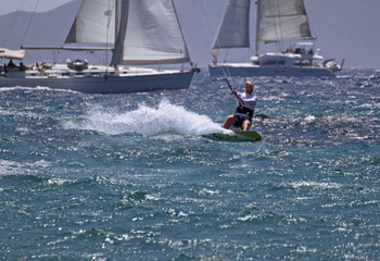 young white male kitesurfing with sailboats behind in aegean sea 