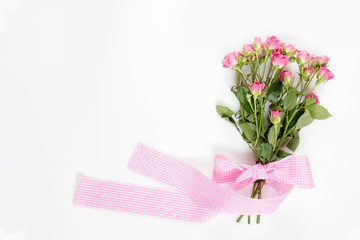 Fresh pink little roses with pink checkered ribbon. Flat lay on white background, top view.