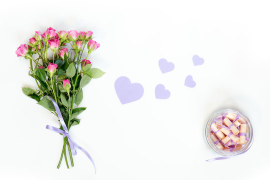 Dreams written on a pink rolled paper in a glass jar, fresh pink little roses and paper violet hearts. Flat lay on white background, top view.
