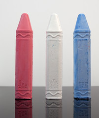 Red, white and blue chalk sticks in the form of crayons on black surface. Vertical.