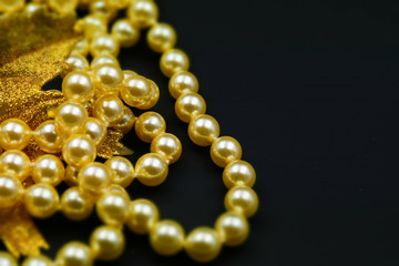 Pearls and glittering golden leaf with black background. Copy space. Tilt-shift effect applied.